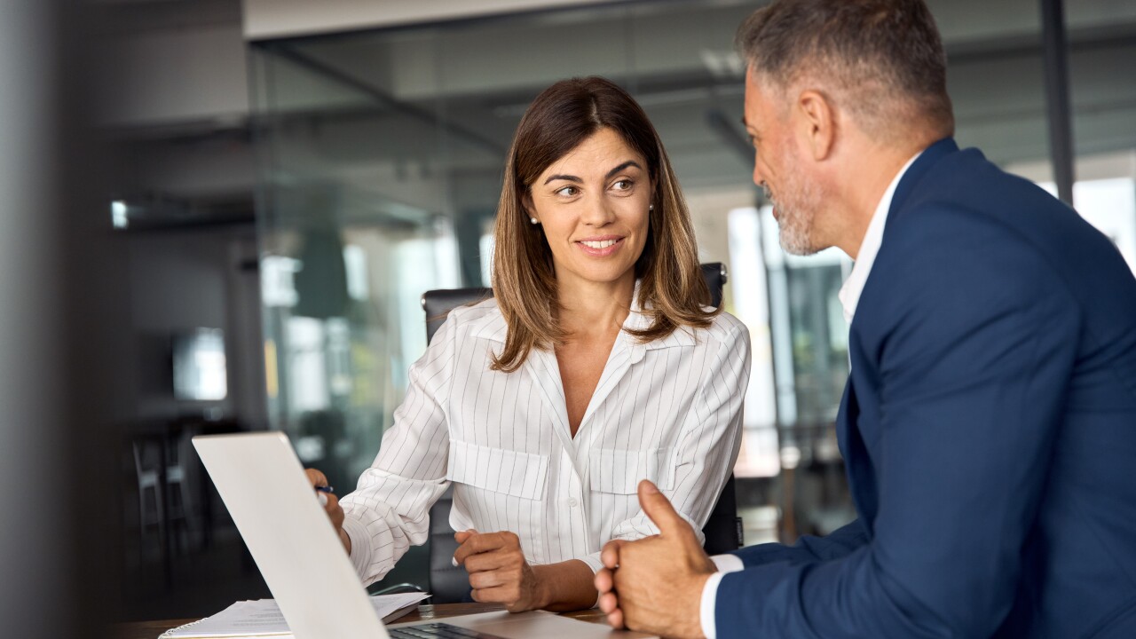 Female and male employee working together on laptop, sitting at table
