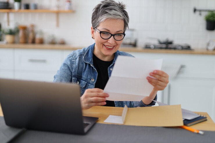 Woman, gray hair and glasses, reading piece of mail at table, smiling