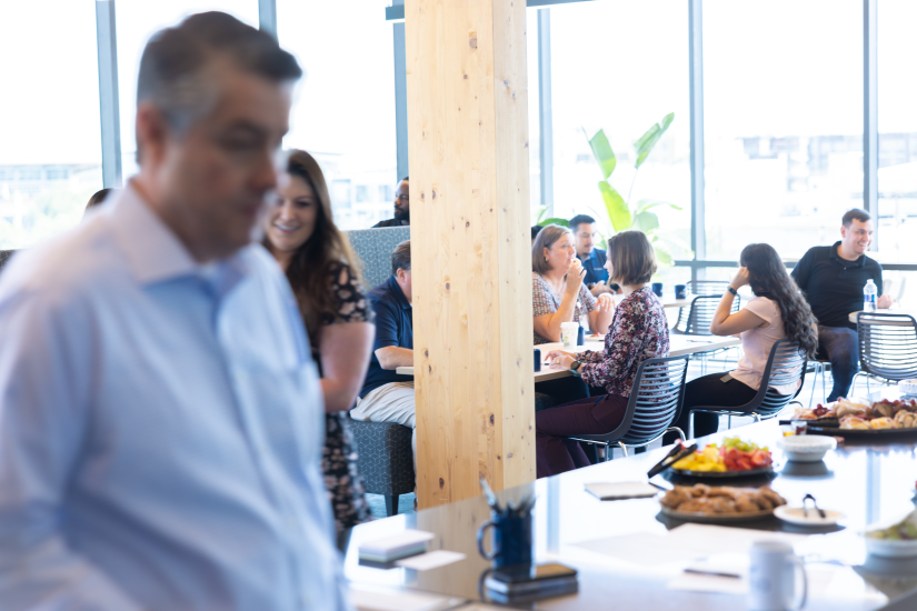 A blurred person with people mingling at a table in the background.
