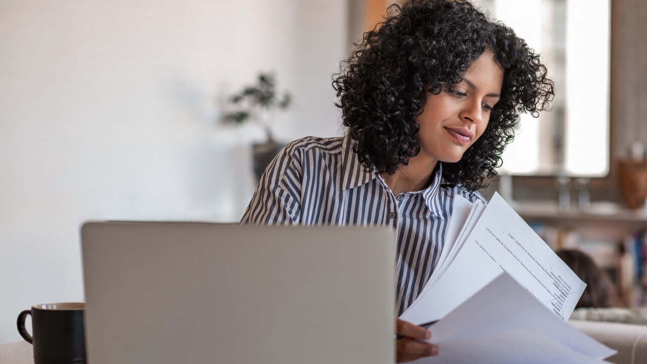 Woman looking over paperwork, sitting in front of laptop computer