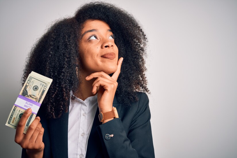 Young woman holding a stack of $20 bills with a quizzical look on her face.