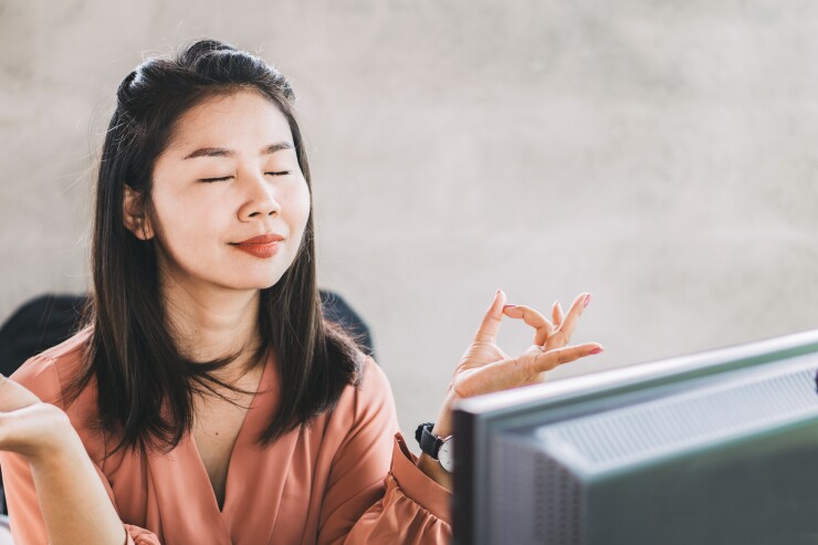 Woman sitting at desk, eyes closed, meditating