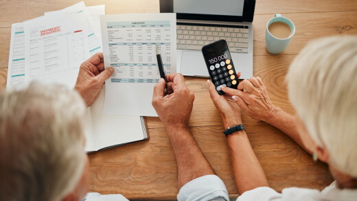 Home budget, finance planning and senior couple calculating their expenses, bills or income during retirement with a calculator, laptop and paper documents from behind. Man and woman discuss savings.