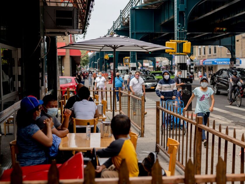 Pedestrians pass in front of customers sitting outside at a restaurant in in the Queens borough of New York.