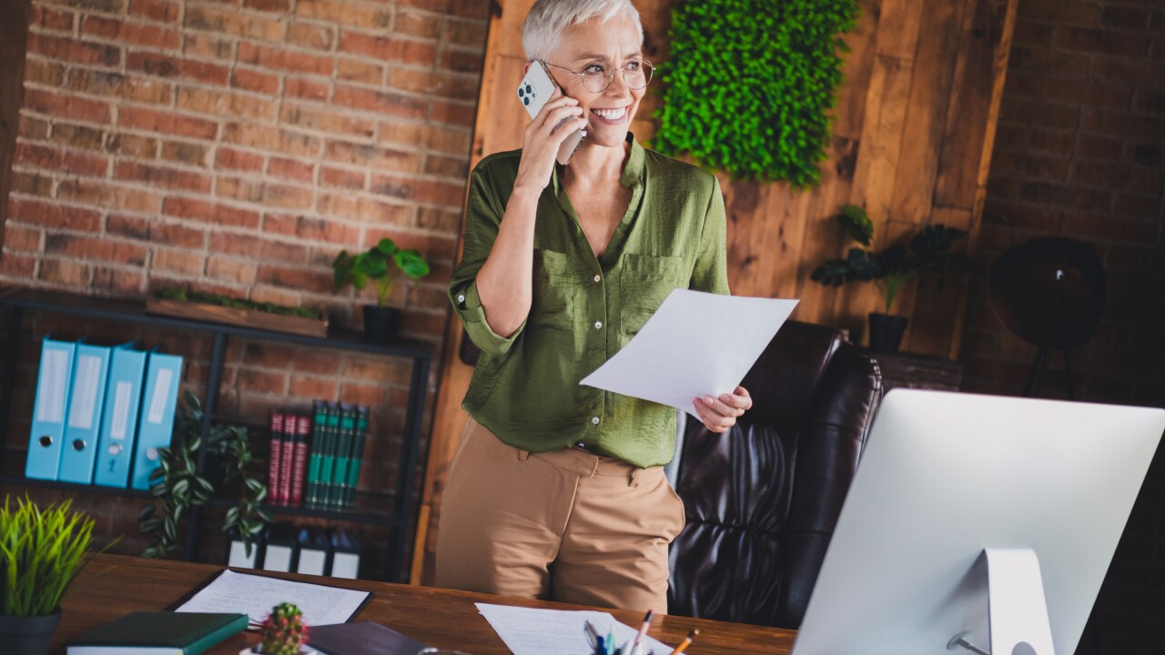 Woman with short gray hair in office talking on phone, holding paper