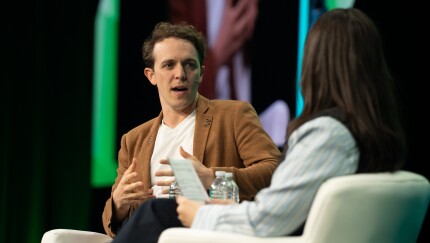 Bolt CEO Ryan Breslow at Fintech Meetup 2026Man in brown jacket and white shirt sits in a chair on a stage, speaking to a female moderator in the foreground.