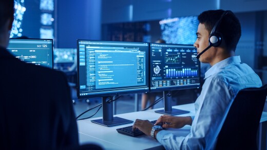 Confident Male Data Scientist Works on Personal Computer Wearing a Headset in Big Infrastructure Control and Monitoring Room. Young Engineer in a Call Center Office Room with Colleagues.