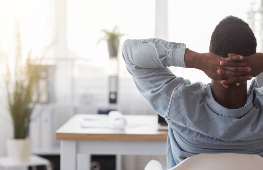 A man leans back on his chair in a sunlit office with plants.