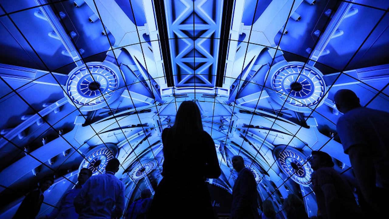 Conference goers walk under a electronic display