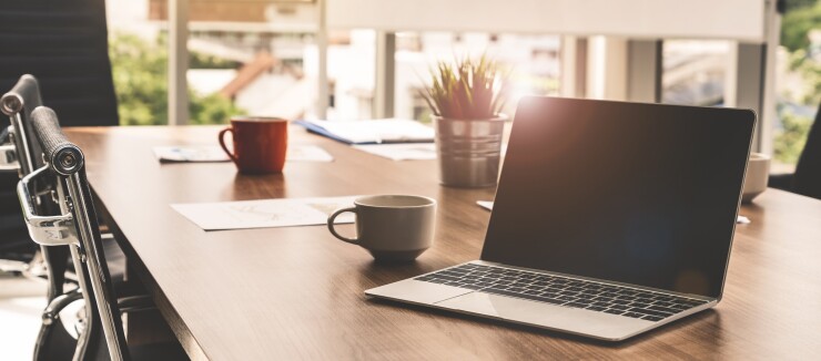 A table with two coffee cups, a plant and a laptop.