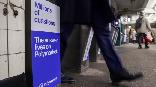 A person walks past a subway turnstile featuring a blue and white Polymarket ad that reads, "Millions of questions. The answer lives on Polymarket."