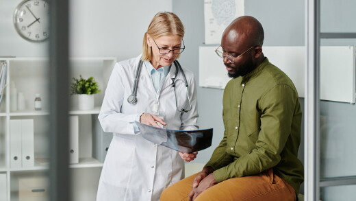 Young adult man wearing glasses and green shirt speaking with female doctor