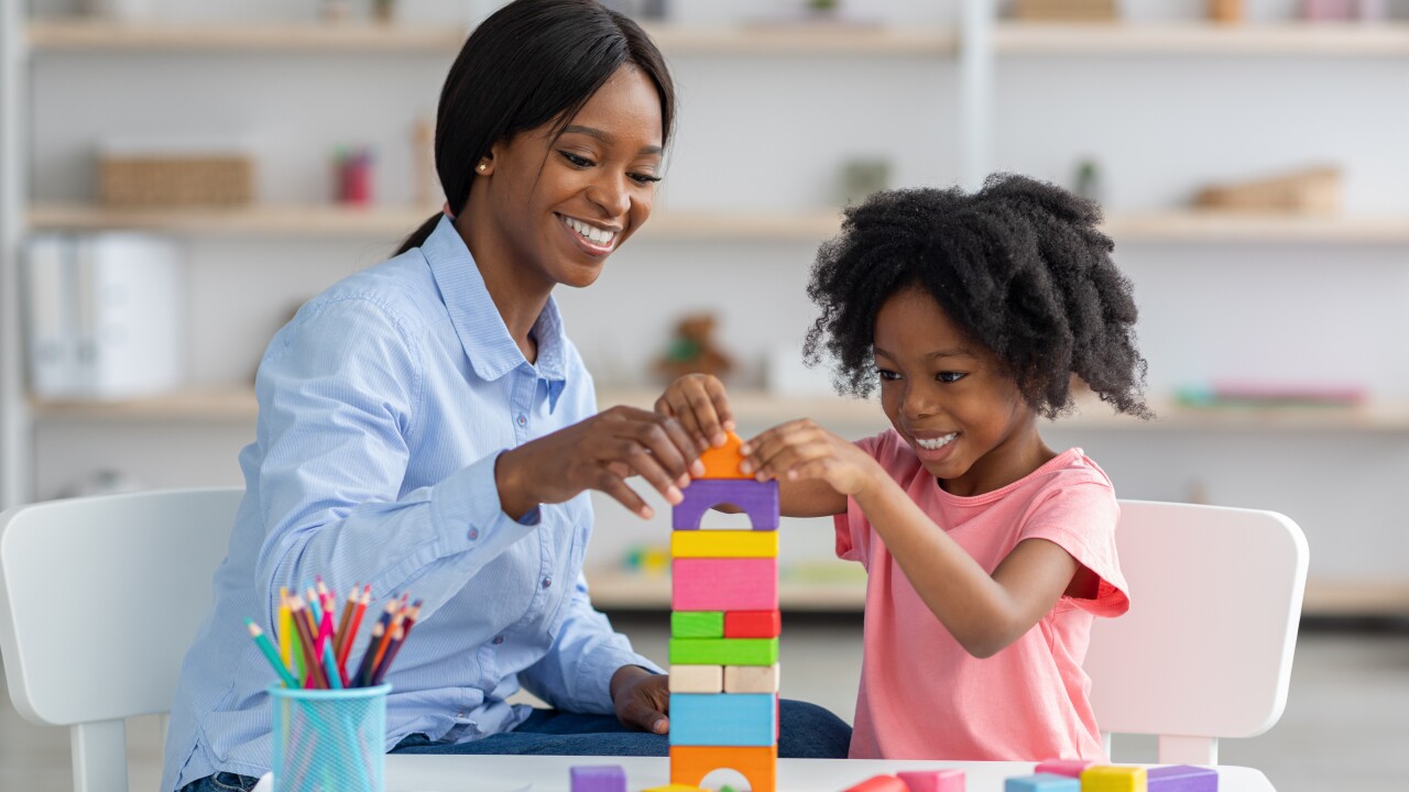 A woman helps a child stack colorful blocks on top of round white table.