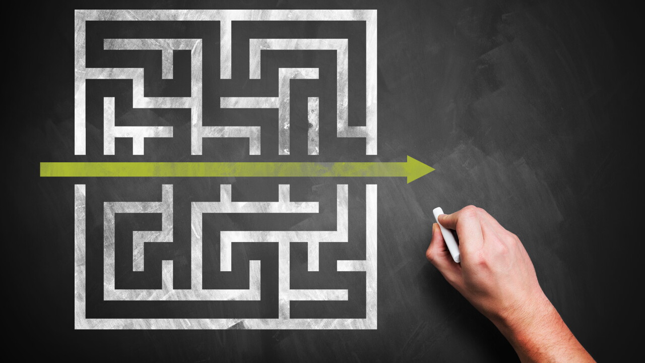 Rendering of a hand drawing a shortcut through a maze on a chalkboard.