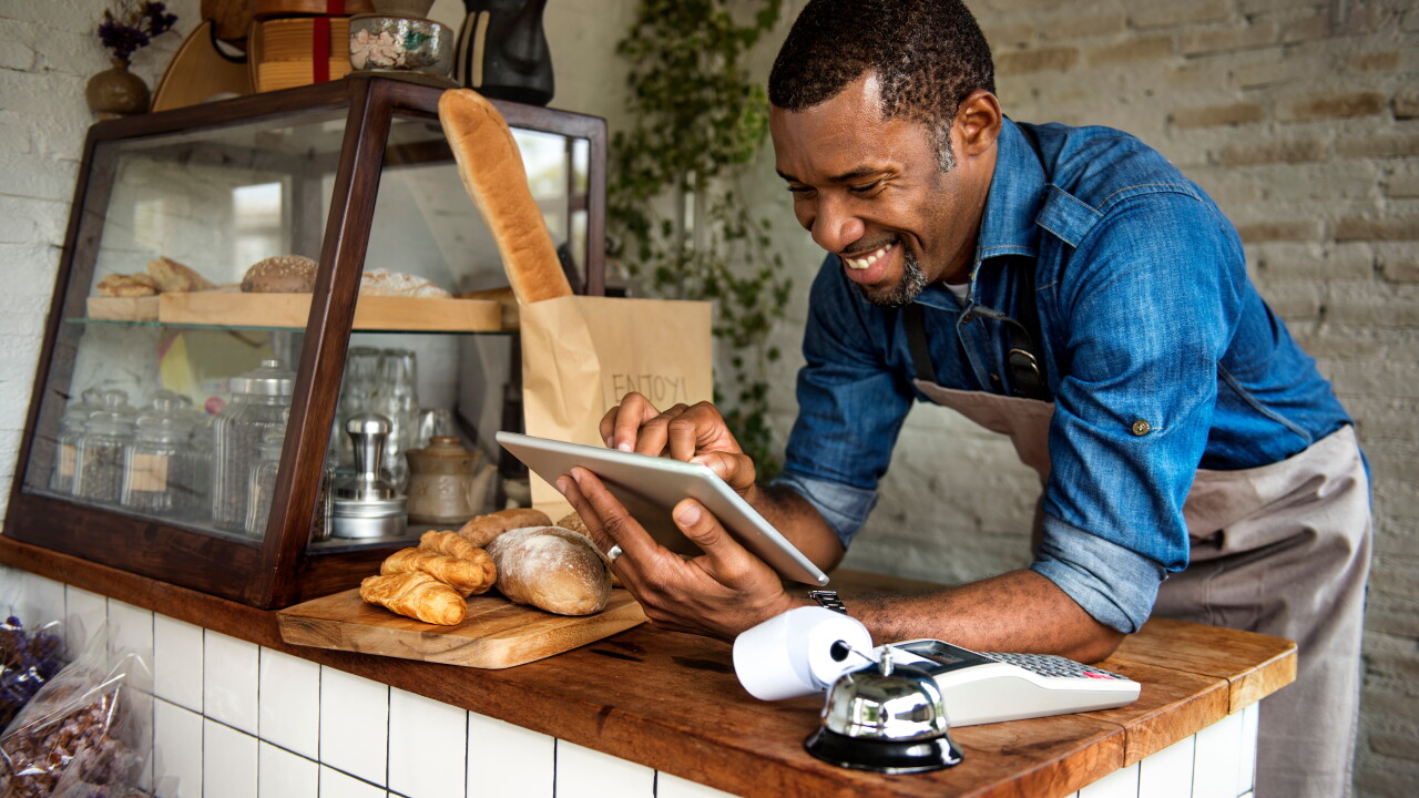 Man leaning on counter of bakery, employee, looking at tablet, smiling, small business