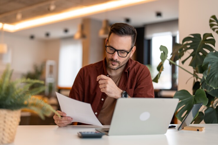 Man, employee, looking at paper while working on computer