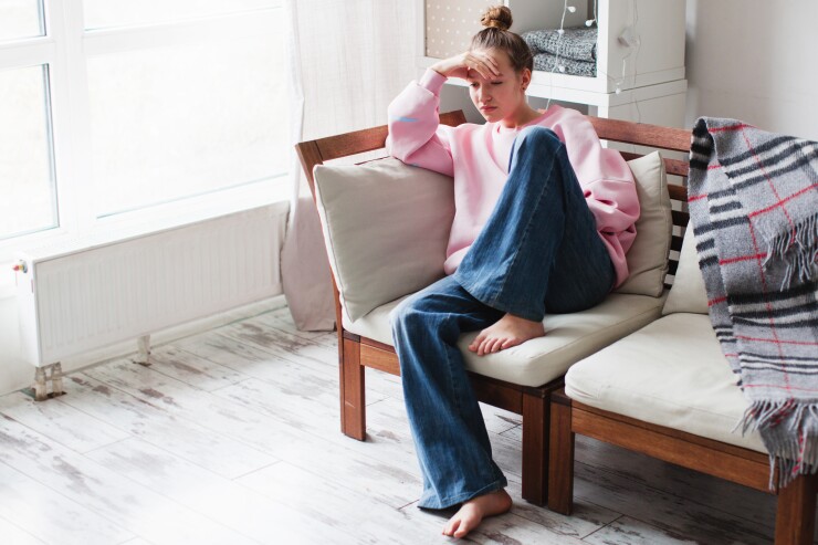 Sad young woman depressed sitting at home on the couch