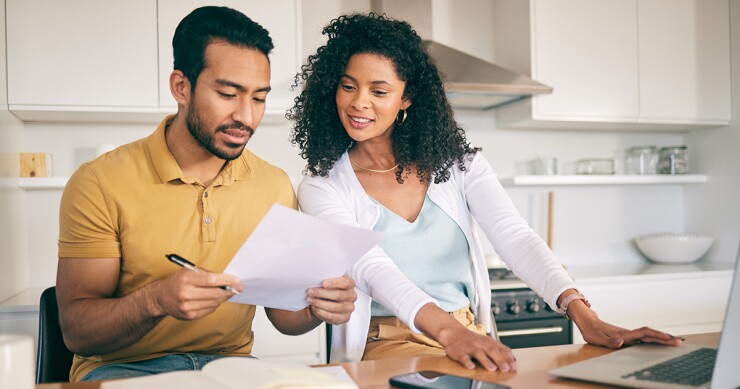 Two people looking at a paper together with a laptop on the counter.