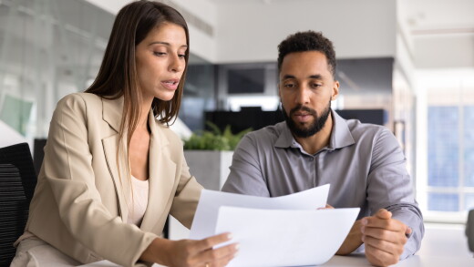 Two employees talking, looking at paperwork, helping