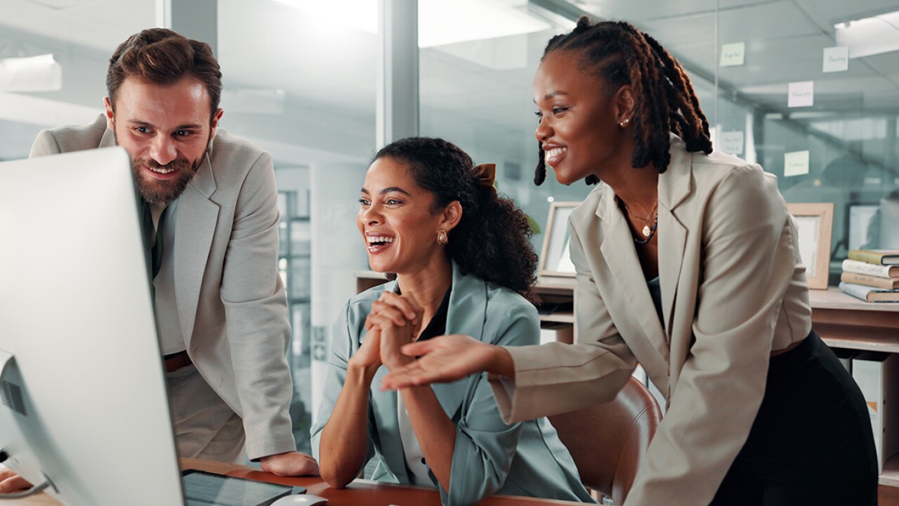 Three people smiling and laughing while looking at a large computer screen.