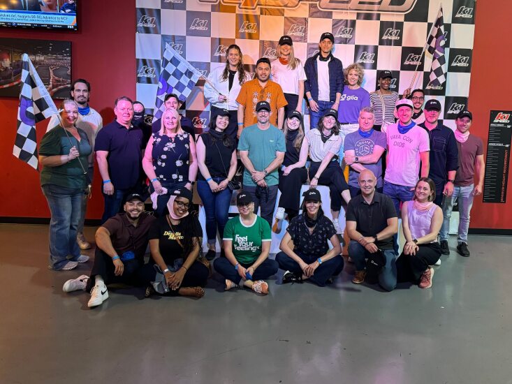 Glia employees at a K1 speed racing track with a white and clack checkered backdrop, with two people holding checkered finish flags.