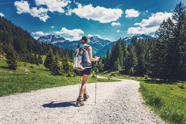 A woman is hiking along a dirt path with mountains looming ahead.