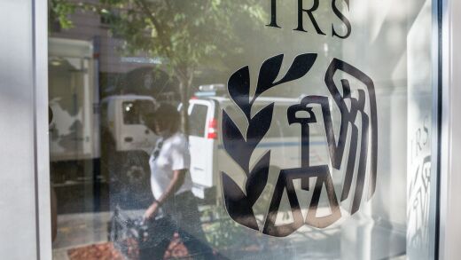 An IRS storefront shows a reflection of parked trucks and a person walking by
