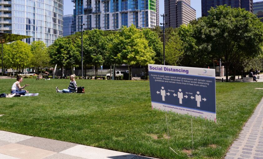 People sit on grass in front of a sign that advises visitors to social distance at Klyde Warren Park in Dallas, Texas, U.S., on Wednesday, April 15, 2020. On Wednesday, Dallas County Health and Human Services reported 1,986 confirmed Covid-19 cases and 43 deaths. Photographer: Rebecca Smeyne/Bloomberg