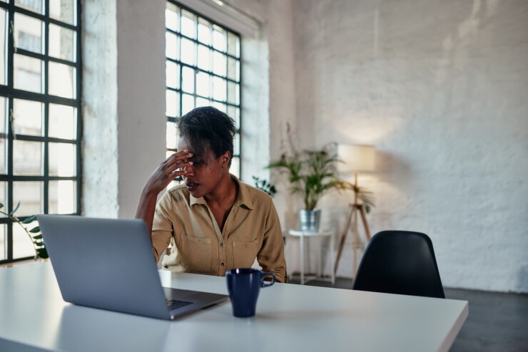 Woman sitting at table with laptop, hand on head, upset, tired