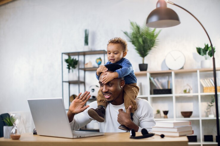 Dad with baby on his shoulders, talking to someone virtually on laptop computer
