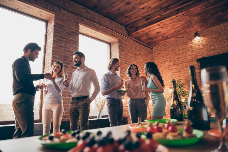 Six colleagues laugh over drinks and food at their company's holiday party.