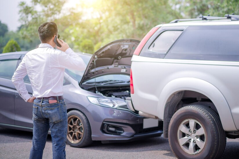 A person using a phone in front of two cars after a rear-end collision.