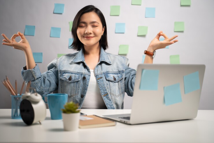 Woman sitting at desk meditating smiling with computer