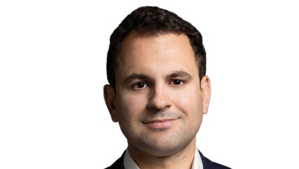 Headshot of Will Peck, a man with short dark hair, wearing a navy blazer and white collared shirt against a white background.
