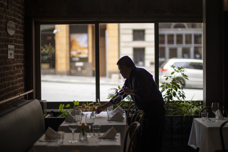 A man is collecting dishes off a table at a restaurant.