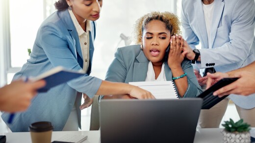 Woman on phone, sitting at desk, surrounded by people, overwhelmed, stressed