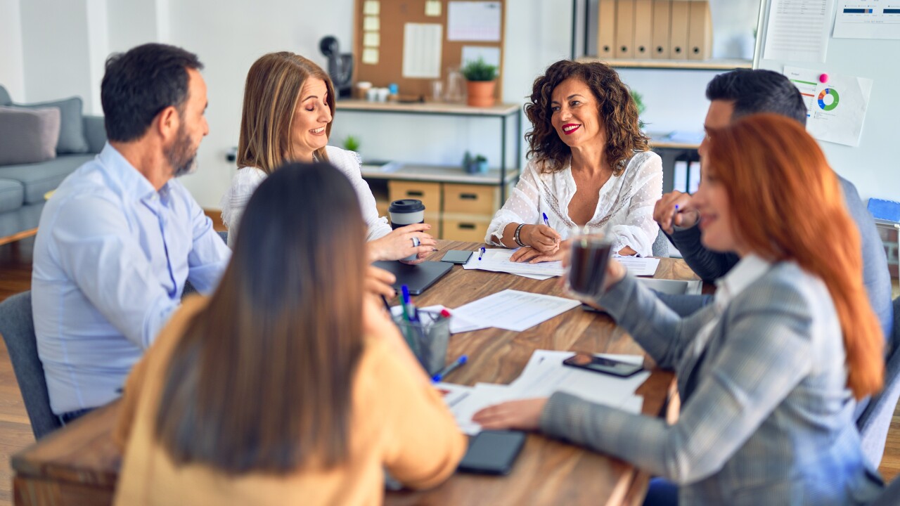 Group of employees talking and smiling around conference table