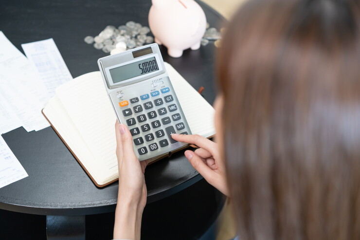 Woman typing on calculator, money and piggy bank on table