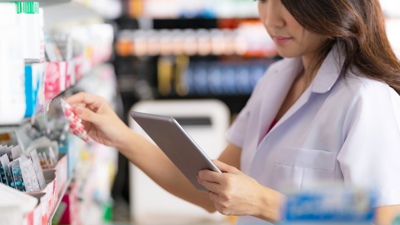 Pharmacist looking at a clip board while putting pills on a shelf