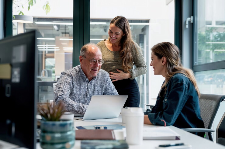 Two women and a man professionally collaborating at a table using a computer.