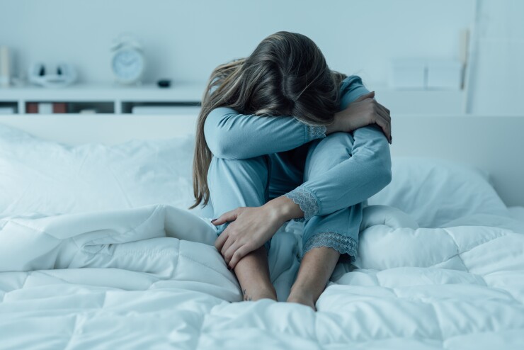 Woman sitting on her bed with her head down