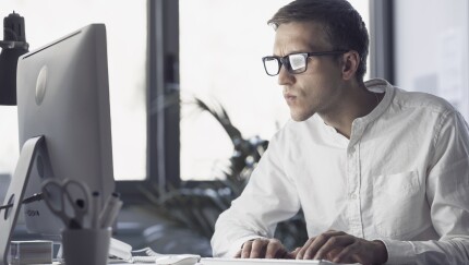 Man with glassses looking at computer screen intently
