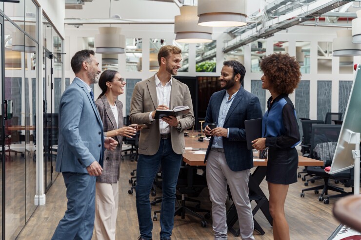 Group of employees standing in office talking and laughing