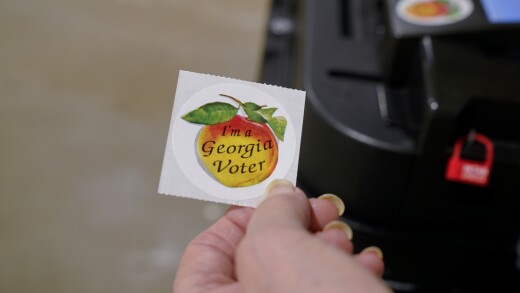 Hand holding sticker with "I'm a Georgia Voter" written on a peach