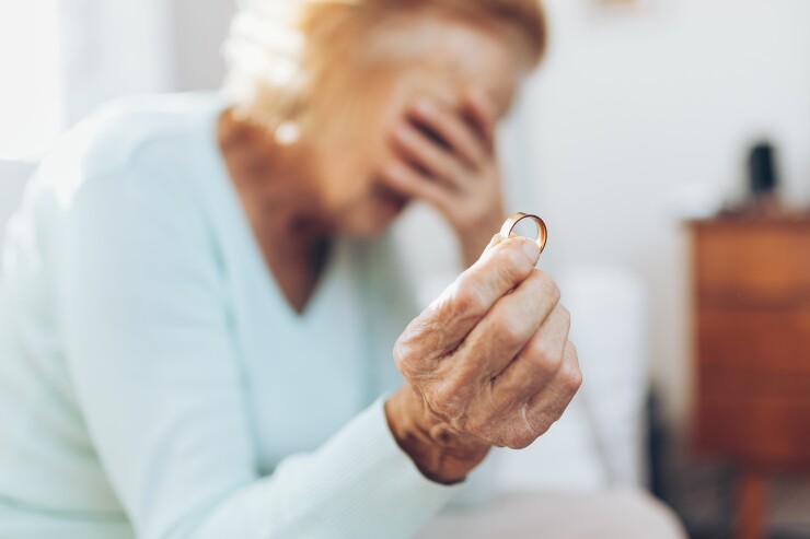 Heartbroken elderly woman holding a wedding ring - gray divorce