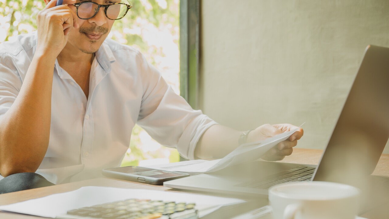 Man with glasses reading paperwork, laptop