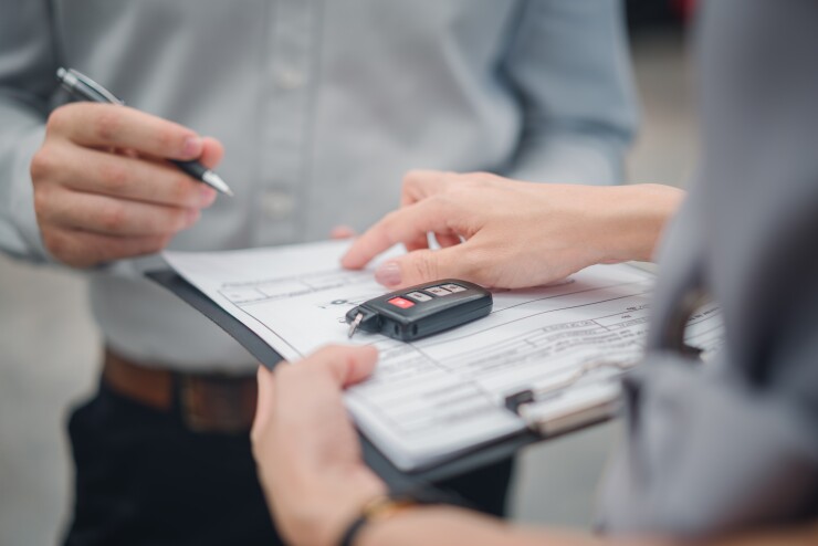 Person with clipboard and car key telling buyer where to sign on form.