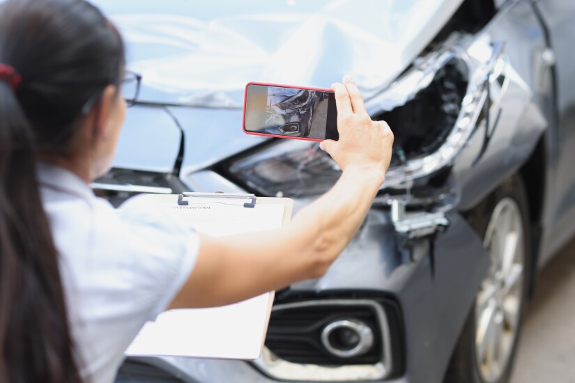 Insurance agent taking pictures of a damaged car on a mobile phone.