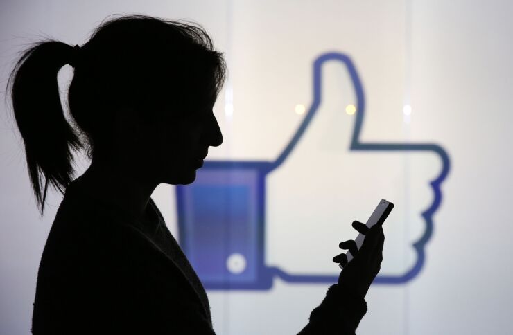 A woman stands holding her smartphone whilst framed against a wall bearing Facebook Inc.s 'Thumbs Up' symbol in this arranged photograph in London, U.K., on Wednesday, Dec. 23, 2015. Facebook Inc.s WhatsApp messaging service, with more than 100 million local users, is the most-used app in Brazil, according to an Ibope poll published on Dec. 15. Photographer: Chris Ratcliffe/Bloomberg