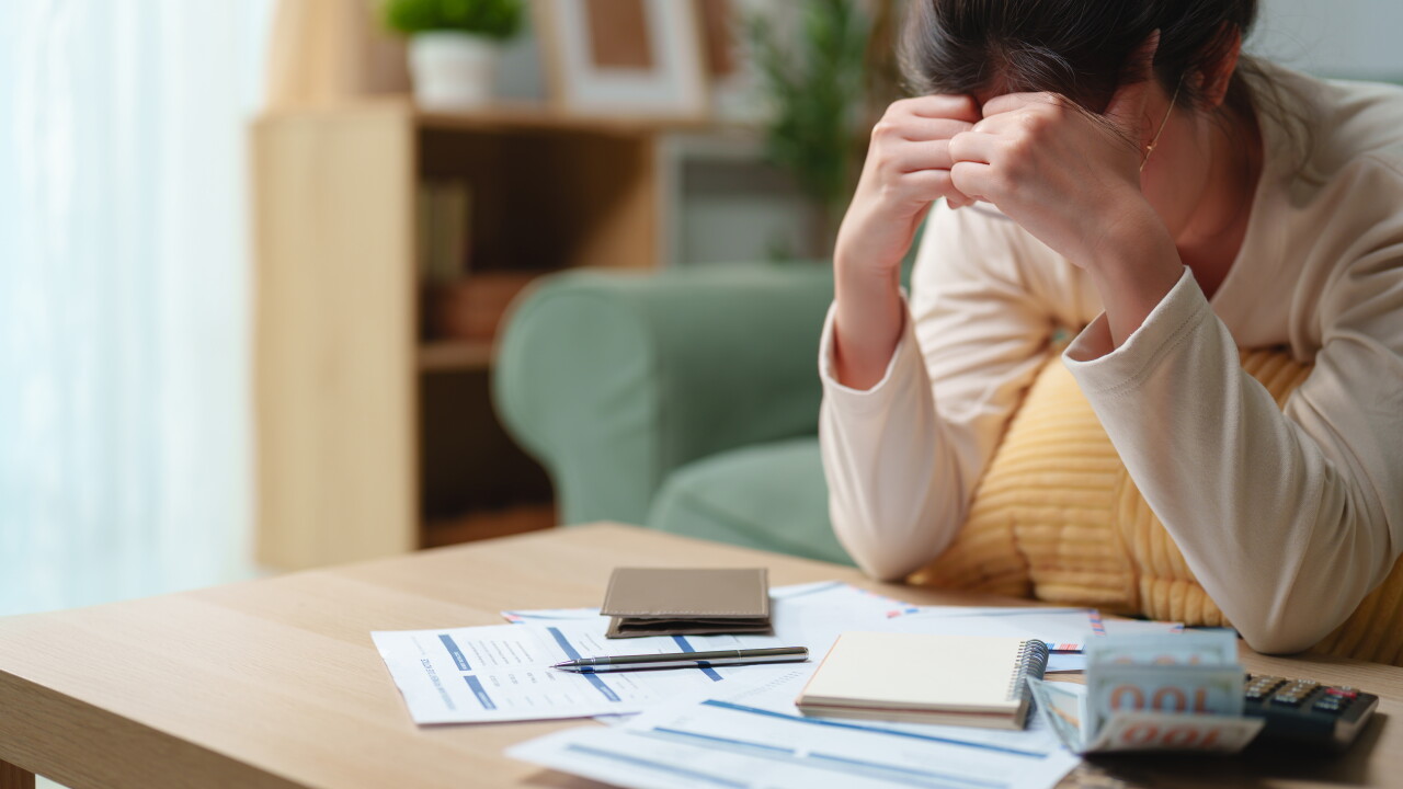 Stressed woman reviewing bills and financial documents at home, feeling worried about debt and monthly expenses. Personal finance, budgeting, financial stress, money problems and economic hardship.